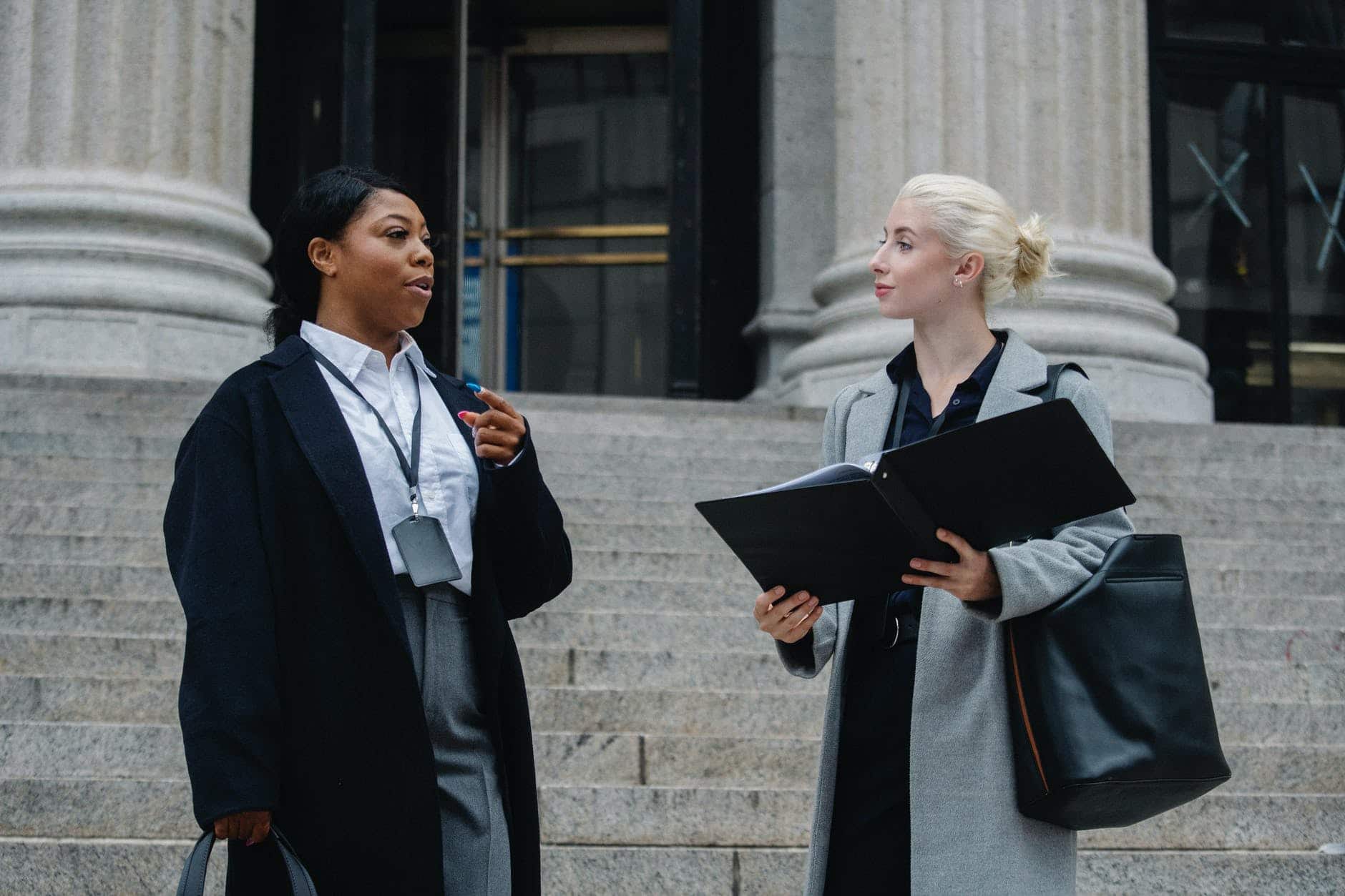 pexels-photo-5669655 elegant diverse female business partners with documents talking on street