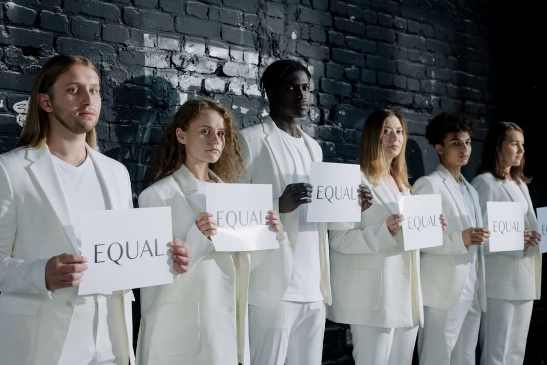 A diverse group of people in white attire holding signs that say 'Equal', promoting equality.